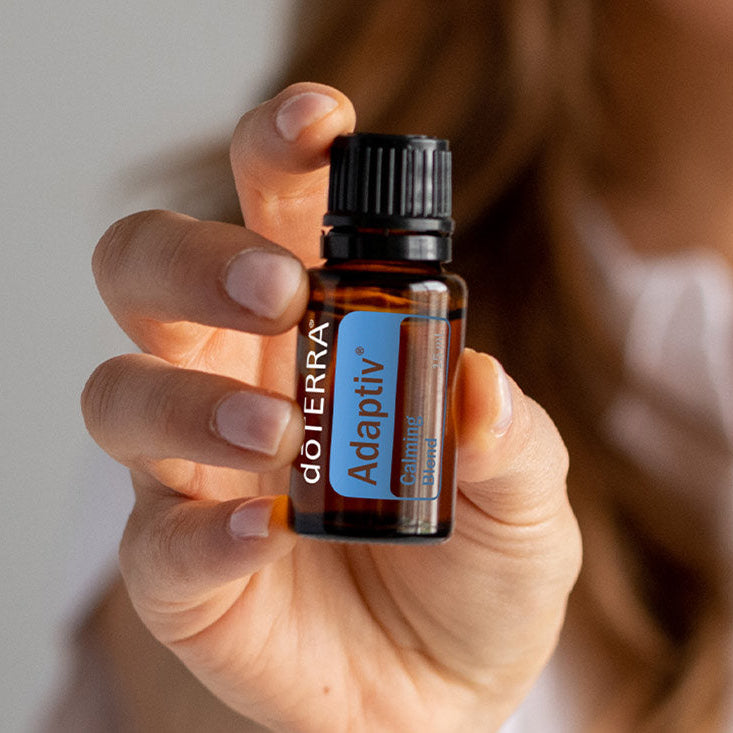 Hand holding a doTERRA Adrenal support essential oil bottle against a neutral background